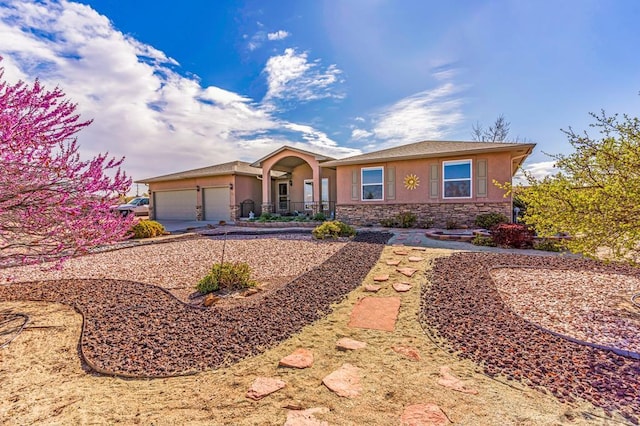 view of front of house featuring a garage, driveway, stone siding, and stucco siding