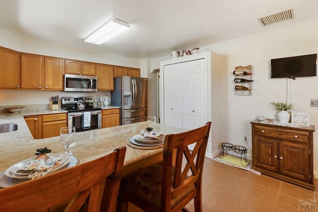 621 Twinflower Dr, Canon City, CO 81212 - kitchen featuring appliances with stainless steel finishes, a breakfast bar, light tile patterned floors, a peninsula, and brown cabinets