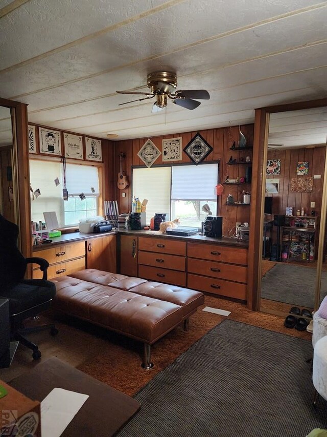 kitchen with wood walls, a textured ceiling, a ceiling fan, and carpet flooring