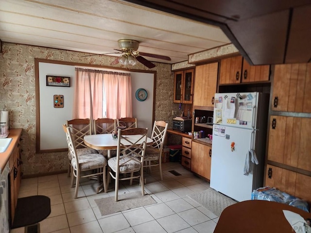 kitchen with wallpapered walls, light tile patterned flooring, brown cabinets, and freestanding refrigerator