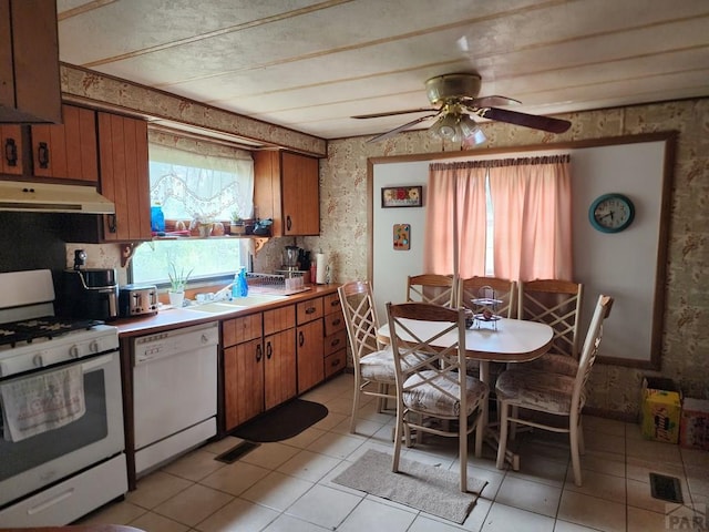 kitchen with light countertops, brown cabinetry, white appliances, under cabinet range hood, and wallpapered walls