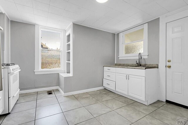 1111 Topaz Pl, Pueblo, CO 81004 - kitchen featuring white gas range oven, a sink, baseboards, white cabinetry, and light tile patterned floors