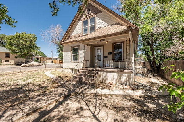 view of front of property featuring a porch, a shingled roof, and fence