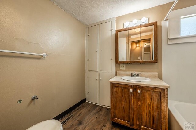 full bath with a textured ceiling, toilet, a bathing tub, wood finished floors, and vanity