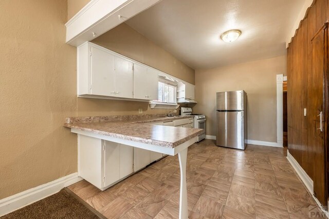 kitchen featuring white range with gas stovetop, white cabinetry, baseboards, light countertops, and freestanding refrigerator