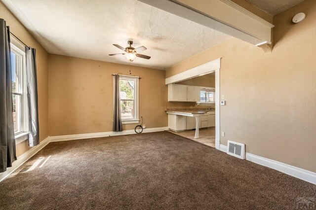 unfurnished living room with ceiling fan, a textured ceiling, light carpet, visible vents, and baseboards