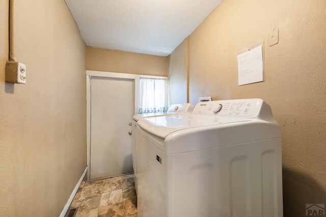 clothes washing area with laundry area, stone finish flooring, baseboards, and washer and dryer