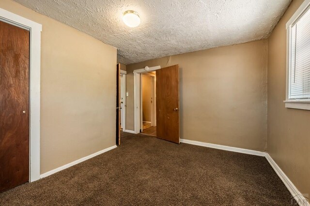 spare room with a textured ceiling, dark colored carpet, and baseboards