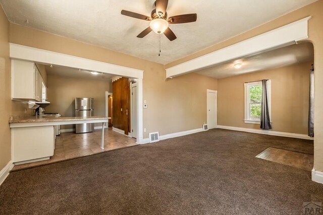 unfurnished living room featuring ceiling fan, baseboards, visible vents, and dark colored carpet