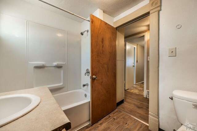 full bathroom with a textured ceiling, toilet, shower / bath combination, wood finished floors, and vanity