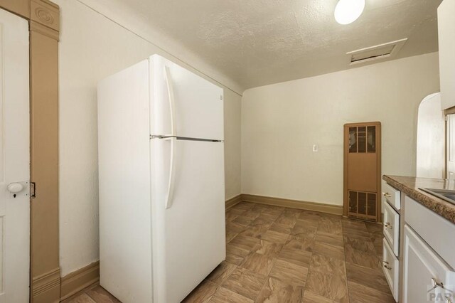 kitchen featuring a textured ceiling, baseboards, freestanding refrigerator, and white cabinets