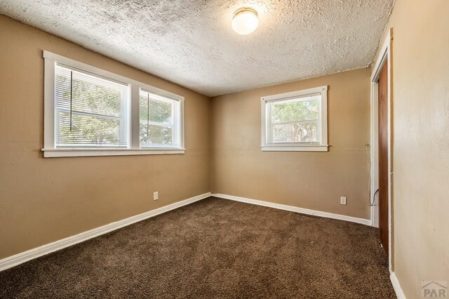 unfurnished room with baseboards, dark colored carpet, and a textured ceiling