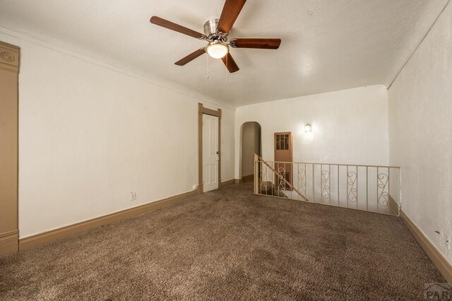 spare room with carpet floors, arched walkways, ceiling fan, and baseboards