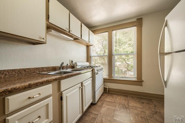 kitchen with dark countertops, white cabinetry, a sink, white appliances, and baseboards