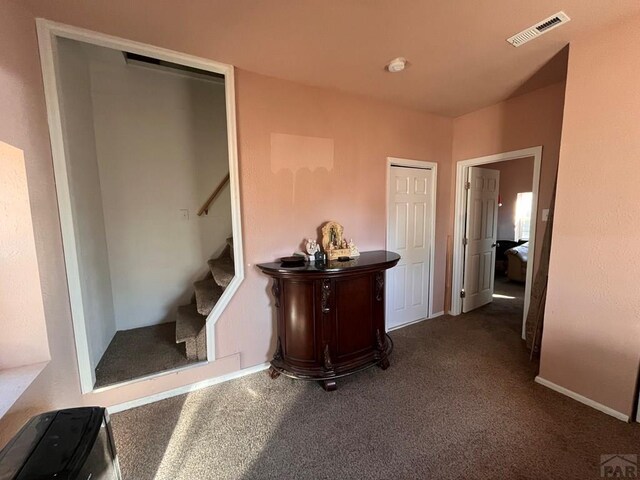 corridor featuring baseboards, stairs, visible vents, and dark carpet