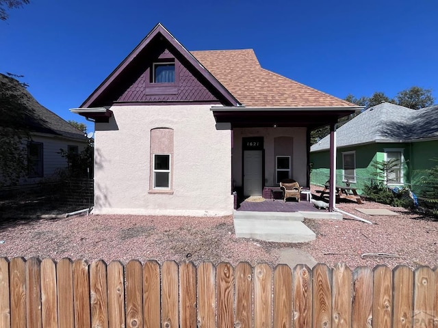 view of front of property with roof with shingles, a patio area, fence, and stucco siding