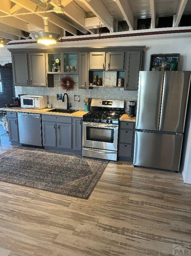 kitchen featuring stainless steel appliances, dark wood-style flooring, a sink, decorative backsplash, and open shelves