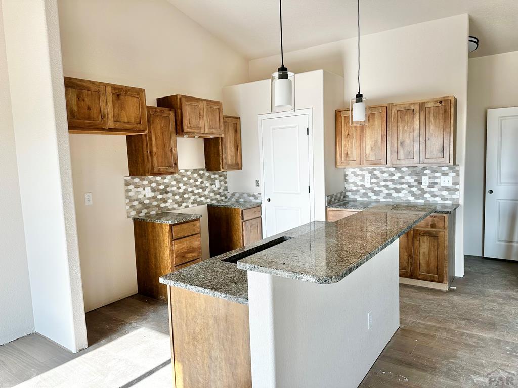 kitchen featuring hanging light fixtures, dark stone countertops, a center island, and brown cabinets