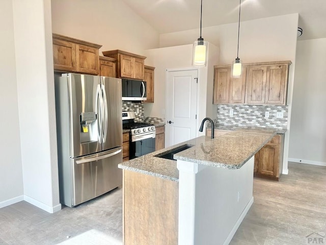 kitchen featuring pendant lighting, light stone counters, brown cabinetry, stainless steel appliances, and a kitchen island with sink