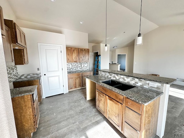 kitchen featuring brown cabinets, hanging light fixtures, backsplash, a sink, and dark stone countertops