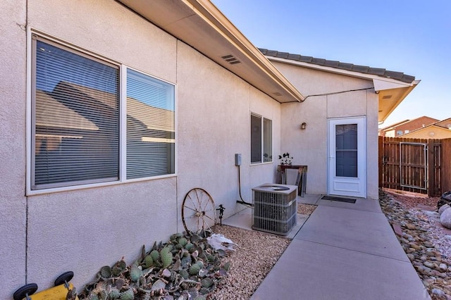 doorway to property featuring stucco siding, central air condition unit, a patio area, and fence