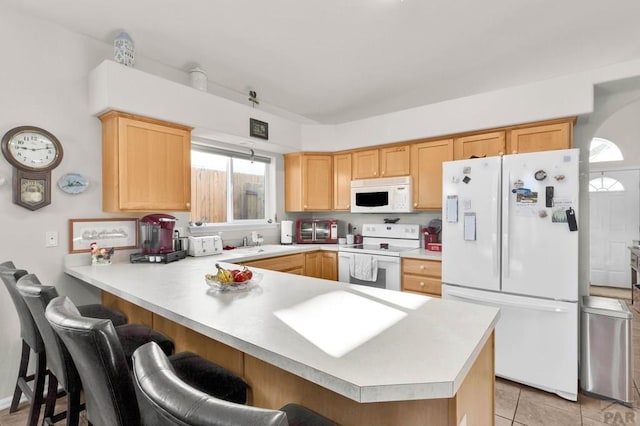 kitchen with white appliances, a peninsula, a sink, light countertops, and a kitchen breakfast bar