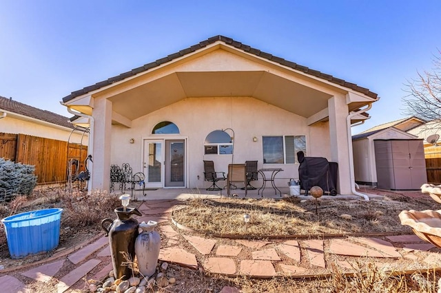 rear view of property with stucco siding, an outbuilding, fence, a storage shed, and a patio area