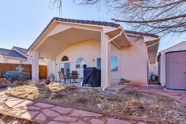 rear view of property featuring a patio, fence, an outbuilding, and stucco siding