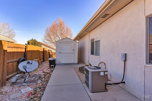 view of patio with a storage shed, cooling unit, fence, and an outbuilding