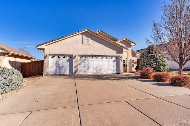 view of front of house featuring fence, an attached garage, stucco siding, concrete driveway, and a tiled roof