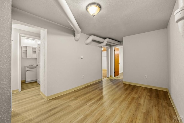 unfurnished room featuring a textured ceiling, a sink, light wood-style flooring, and baseboards