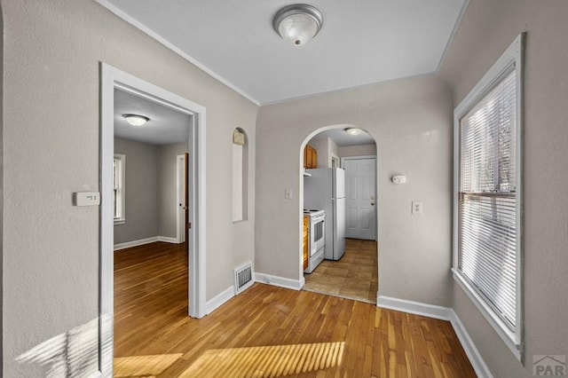 interior space featuring arched walkways, baseboards, visible vents, and light wood finished floors