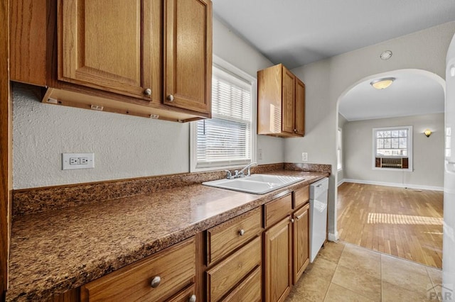 kitchen with light tile patterned floors, arched walkways, a sink, dishwasher, and dark countertops