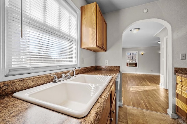 kitchen with arched walkways, brown cabinets, a sink, and light tile patterned flooring