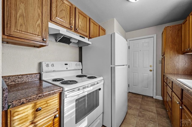 kitchen featuring white appliances, dark tile patterned floors, brown cabinets, and under cabinet range hood