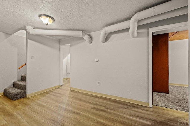 below grade area with baseboards, a textured ceiling, stairway, and wood finished floors