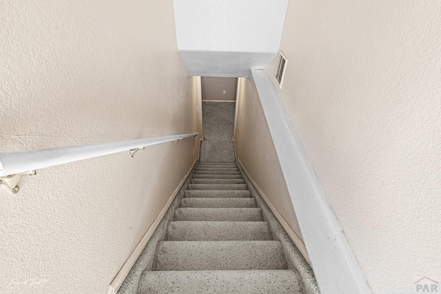 stairway featuring carpet floors, visible vents, and a textured wall