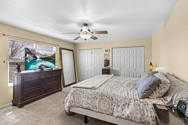 bedroom with light carpet, ceiling fan, baseboards, and multiple closets