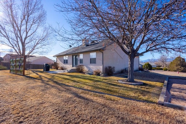 view of front of home featuring a front lawn, a chimney, fence, and stucco siding