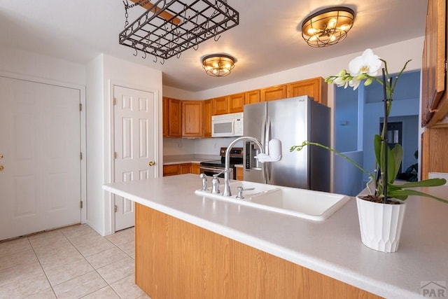 kitchen with light tile patterned floors, stainless steel appliances, a sink, light countertops, and brown cabinetry