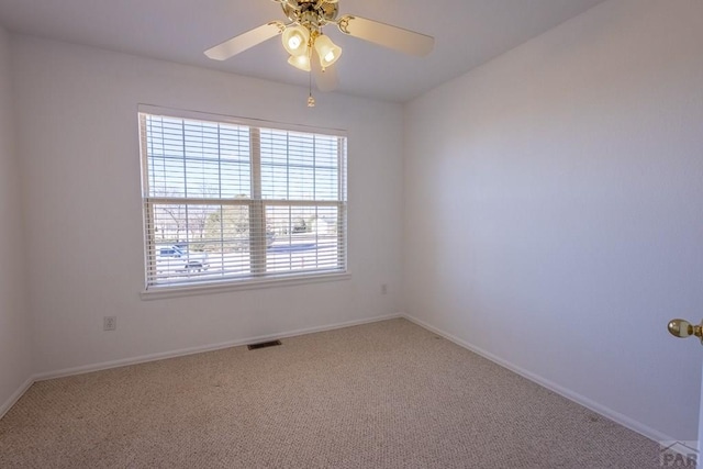 carpeted spare room with baseboards, visible vents, and a ceiling fan