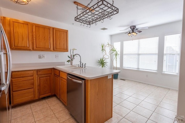 kitchen featuring appliances with stainless steel finishes, a peninsula, light countertops, a sink, and light tile patterned flooring