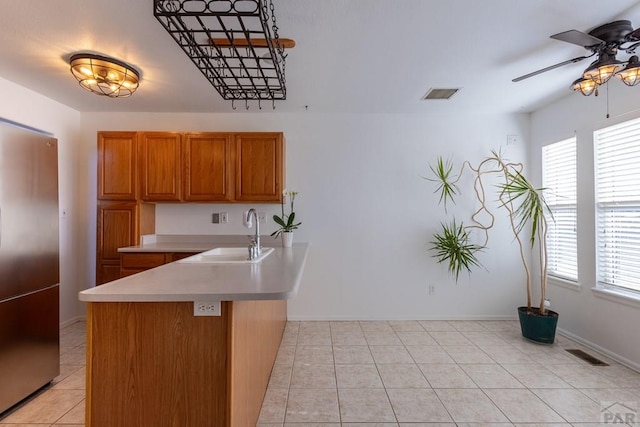 kitchen featuring a sink, brown cabinetry, stainless steel refrigerator, and visible vents