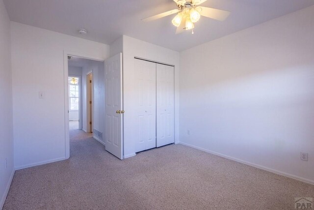 unfurnished bedroom featuring a ceiling fan, a closet, light carpet, and baseboards