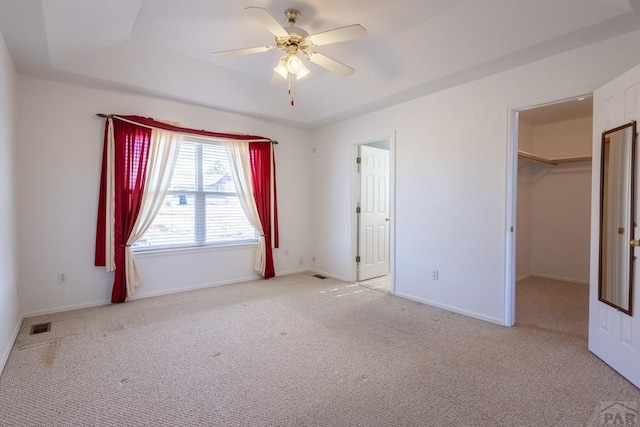 unfurnished bedroom featuring carpet floors, visible vents, baseboards, a walk in closet, and a raised ceiling