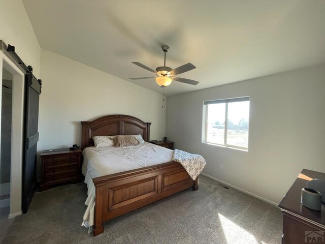 bedroom featuring dark colored carpet, a barn door, a ceiling fan, and baseboards