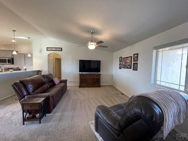 living room with arched walkways, light colored carpet, lofted ceiling, and baseboards