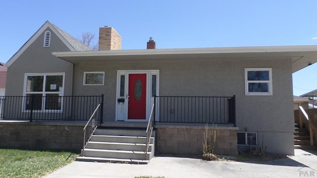 view of front facade featuring a porch, stucco siding, stairs, and a chimney