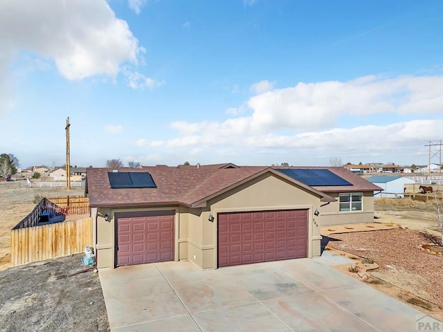 single story home with stucco siding, an attached garage, roof mounted solar panels, fence, and driveway