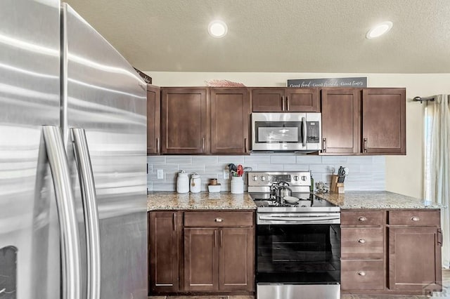 kitchen featuring tasteful backsplash, appliances with stainless steel finishes, light stone countertops, a textured ceiling, and recessed lighting